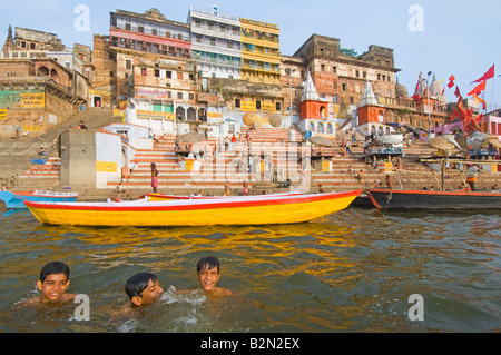 Ampio angolo di visione di persone sulla Ahilyabai Ghat eseguendo il loro rito quotidiano con 3 happy giovani nuotatori in primo piano. Foto Stock