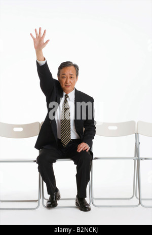 Ritratto di un imprenditore seduto su una sedia con la mano alzata Foto Stock