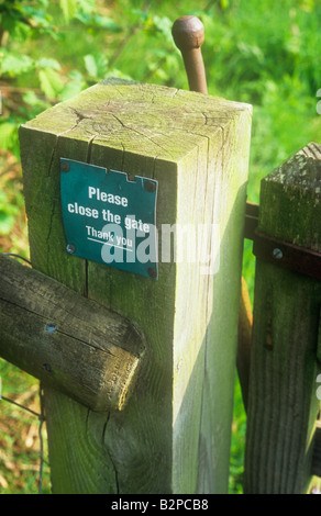 Dettaglio di gatepost con chiusura cancello di fattoria e il fogliame verde al di là con plastica incrinate segno si prega di chiudere la porta grazie Foto Stock