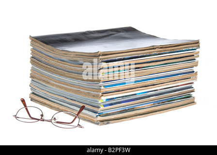 Una pila di vecchie riviste usurate con gli occhiali da lettura isolata contro uno sfondo bianco Foto Stock