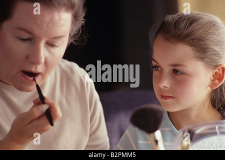 Ragazza 8 anni a guardare la sua madre applicare il rossetto per labbra Foto Stock