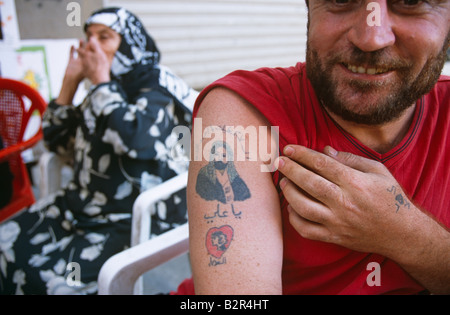 Uomo in mostra il suo tatuaggio, donna in sedia in background, Beirut, Libano Foto Stock