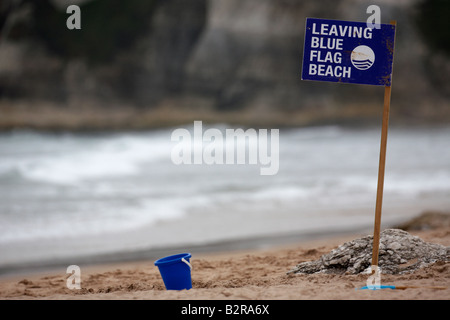 Lasciando spiaggia bandiera blu con segno blu abbandonati childs secchio di plastica su rocce bianche beach County Antrim Irlanda del Nord Foto Stock