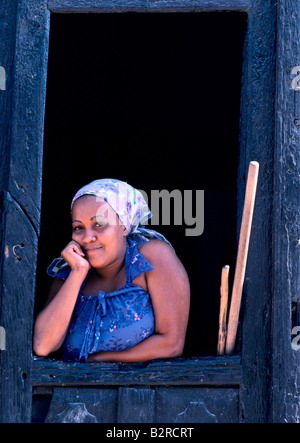 Giovane donna cubana indossando un velo, guardando fuori da una cornice di legno in una porta, sorridente alla fotocamera in Trinidad, Cuba Foto Stock
