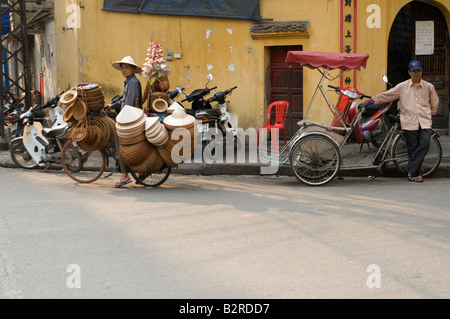 Hat venditore e un ciclo taxi driver guardando la telecamera nel quartiere vecchio di Hanoi, Vietnam Foto Stock
