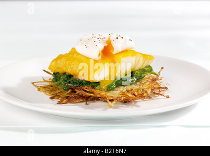 Il pesce bianco con soft uovo in camicia su letto di foglie verdi e filamenti di patate Foto Stock