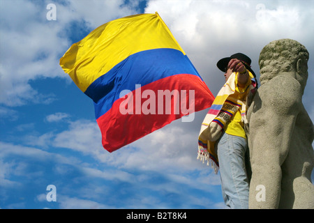 Uomo colombiano branding il colombiano bandiera con una statua nella sua parte posteriore e il cielo in background Foto Stock