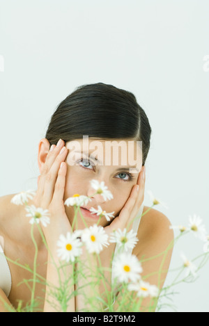 La donna dietro la pianta di camomilla, tenendo la testa, guardando in alto Foto Stock