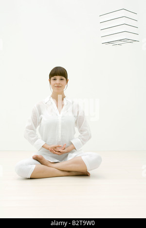 Donna seduta in posizione meditativa, sorridente in telecamera Foto Stock