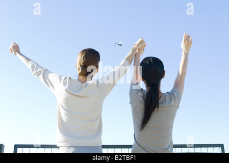 Due donne guardando l'aereo nel cielo, tenendo le mani, braccia alzate, vista posteriore Foto Stock