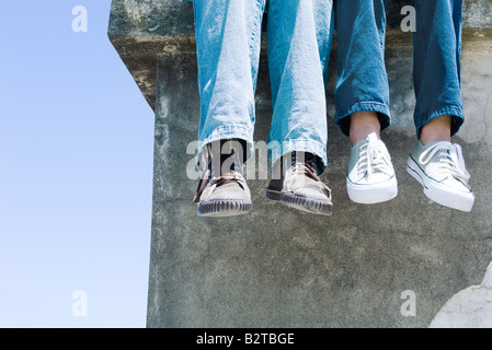 Due coppie di gambe penzolanti sulla mensola di calcestruzzo Foto Stock