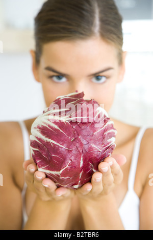 Donna che mantiene una testa di radicchio lattuga, occultato parzialmente il suo volto, guardando la fotocamera Foto Stock