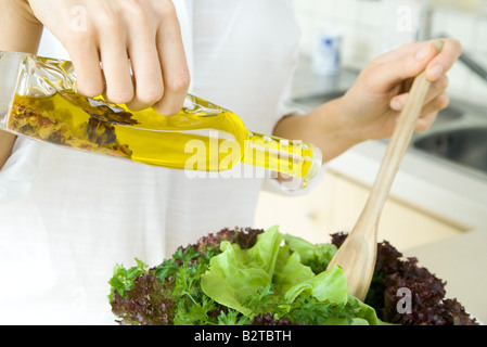 Donna versando olio d'oliva Il condimento sull'insalata, vista ritagliata Foto Stock