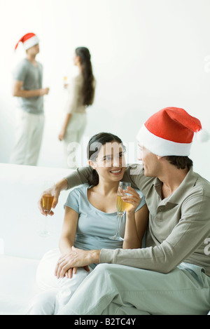 Giovane seduto sul divano, bevendo champagne, uomo che indossa Santa hat Foto Stock