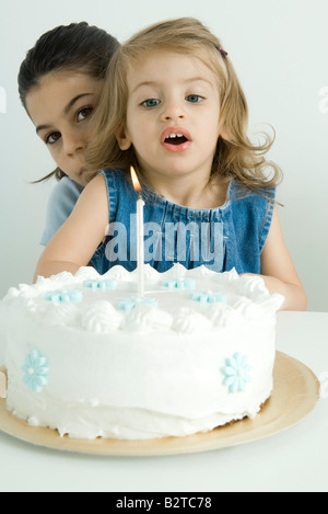 Ragazza soffiando fuori candela sulla torta di compleanno e suor sbirciare fotocamera da dietro Foto Stock