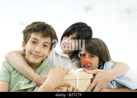 Madre con bracci intorno i due figli di lei, uno che indossa clown naso, ritratto Foto Stock