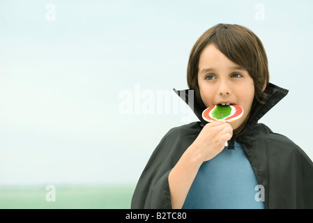 Ragazzo che indossa vampire cape, mangiando grandi lecca-lecca, ritratto Foto Stock