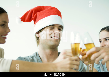 Amici adulti tintinnanti bicchieri da champagne, sorridente, concentrarsi sull'uomo in Santa hat, ritagliato Foto Stock