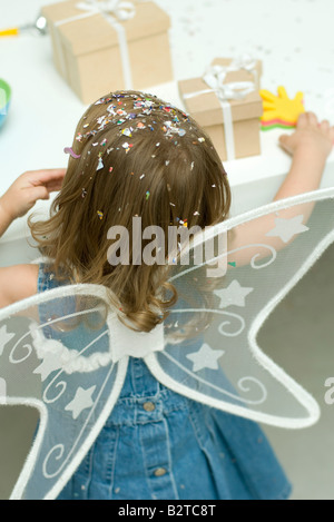 Bambina indossa ali, coriandoli nei suoi capelli, vista posteriore Foto Stock