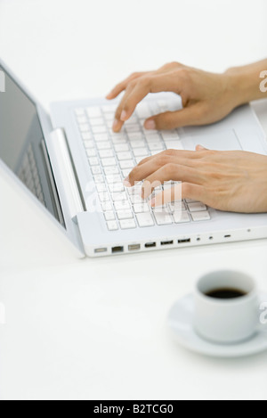 Le mani la digitazione su computer portatile, tazza di caffè in primo piano Foto Stock