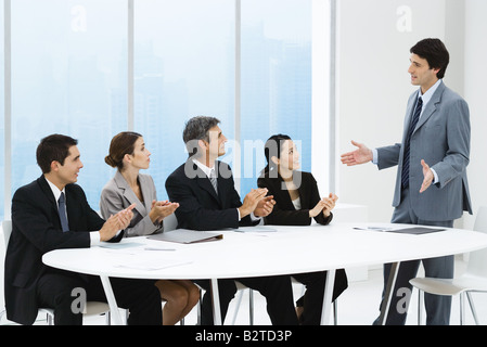 La gente di affari ad applaudire associare la presentazione, seduti attorno al tavolo di gioco Foto Stock