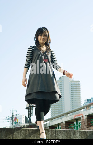 Giovane donna a piedi nella cornice urbana, sorridente in telecamera a basso angolo di visione Foto Stock