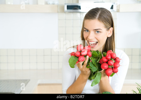 Donna che mantiene fino a grappoli di freschi ravanelli, sorridente in telecamera Foto Stock