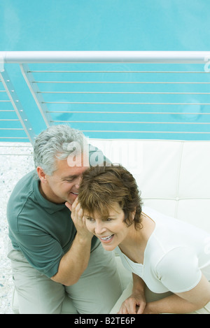 Giovane seduti sul balcone, uomo whispering nella donna di orecchio, ad alto angolo di visione Foto Stock