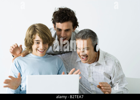 Padre e i due figli guardando al computer portatile insieme, sorridente, mani sollevate Foto Stock