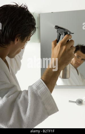 Uomo che guarda a se stesso in uno specchio, spritzing capelli con la bottiglia spray Foto Stock