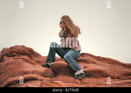 Una giovane donna siede su un rocce costiere che guarda al mare. Foto Stock
