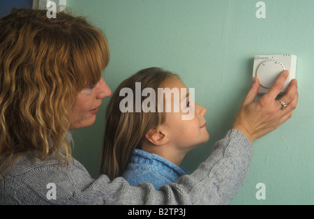 Madre figlia che mostra come ruotare verso il basso il riscaldamento del termostato Foto Stock