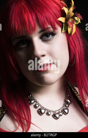 Headshot ritratto di una giovane donna di goth con luminosi capelli rossi e un fiore giallo tra i capelli. Foto Stock