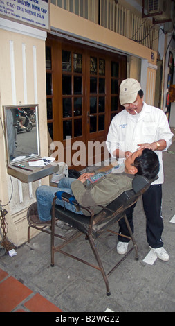 Marciapiede barbiere rade uomo in sedia marciapiede Hanoi Vietnam Foto Stock