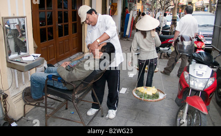 Marciapiede barbiere rade uomo in sedia marciapiede Hanoi Vietnam Foto Stock