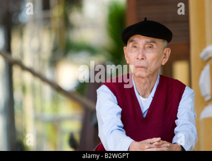 Anziani uomo vietnamita vestita di nero francese beret si siede in street Hoi An Vietnam Foto Stock