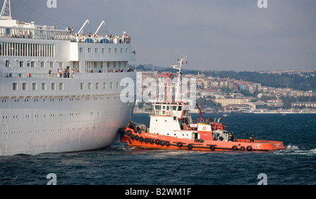 Spingere intorno a. Una luce arancione brillante rimorchiatore spinge a poppa di un bianco grande nave da crociera per portare in porto passeggeri watch Foto Stock