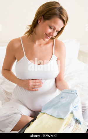 Donna incinta di imballaggio abbigliamento bambino in valigia sorridente Foto Stock