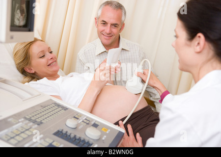 Donna incinta ricevendo ultrasuoni dal medico con il marito guardando foto Foto Stock