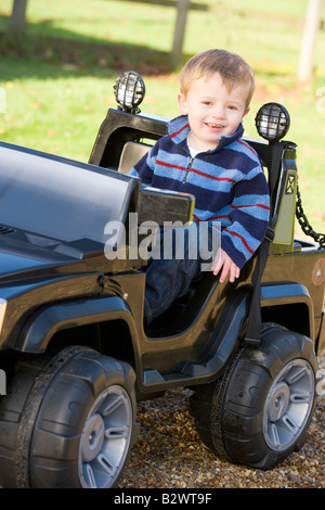 Giovane ragazzo giocando all'aperto in giocattolo carrello sorridente Foto Stock