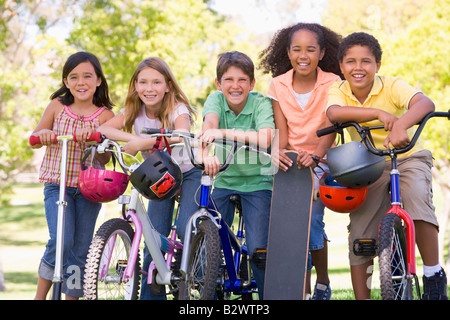 Cinque giovani amici con le biciclette scooter e skateboard sorride all'aperto Foto Stock