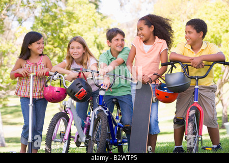 Cinque giovani amici con le biciclette scooter e skateboard sorride all'aperto Foto Stock