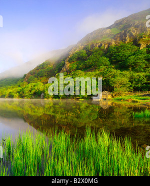 Un piccolo boathouse su una calma splendidamente e nebbiosa mattina a Llyn Dinas nel parco nazionale di Snowdonia nel Galles del Nord Foto Stock