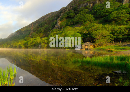 Un piccolo boathouse su una calma splendidamente e nebbiosa mattina a Llyn Dinas nel parco nazionale di Snowdonia nel Galles del Nord Foto Stock