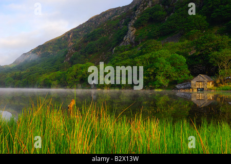 Un piccolo boathouse su una calma splendidamente e nebbiosa mattina a Llyn Dinas nel parco nazionale di Snowdonia nel Galles del Nord Foto Stock