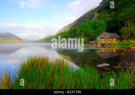 Un piccolo boathouse su una calma splendidamente e nebbiosa mattina a Llyn Dinas nel parco nazionale di Snowdonia nel Galles del Nord Foto Stock