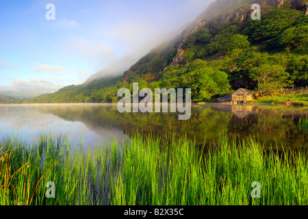 Un piccolo boathouse su una calma splendidamente e nebbiosa mattina a Llyn Dinas nel parco nazionale di Snowdonia nel Galles del Nord Foto Stock