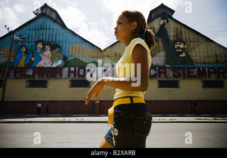 Una ragazza cammina passato un murale raffigurante Fidel Castro e una famiglia cubana di Santiago di Cuba - Foto Stock