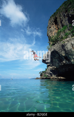 Giovane all'aperto salta fuori da scogliera in ocean Foto Stock