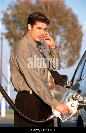 L'uomo il pompaggio del gas mentre parlano al telefono cellulare al self service stazione di benzina in California Foto Stock